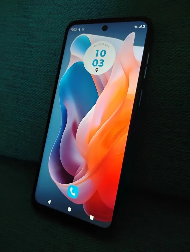 A real phone on a dark green couch. The home screen has a clock and a single app icon on it.